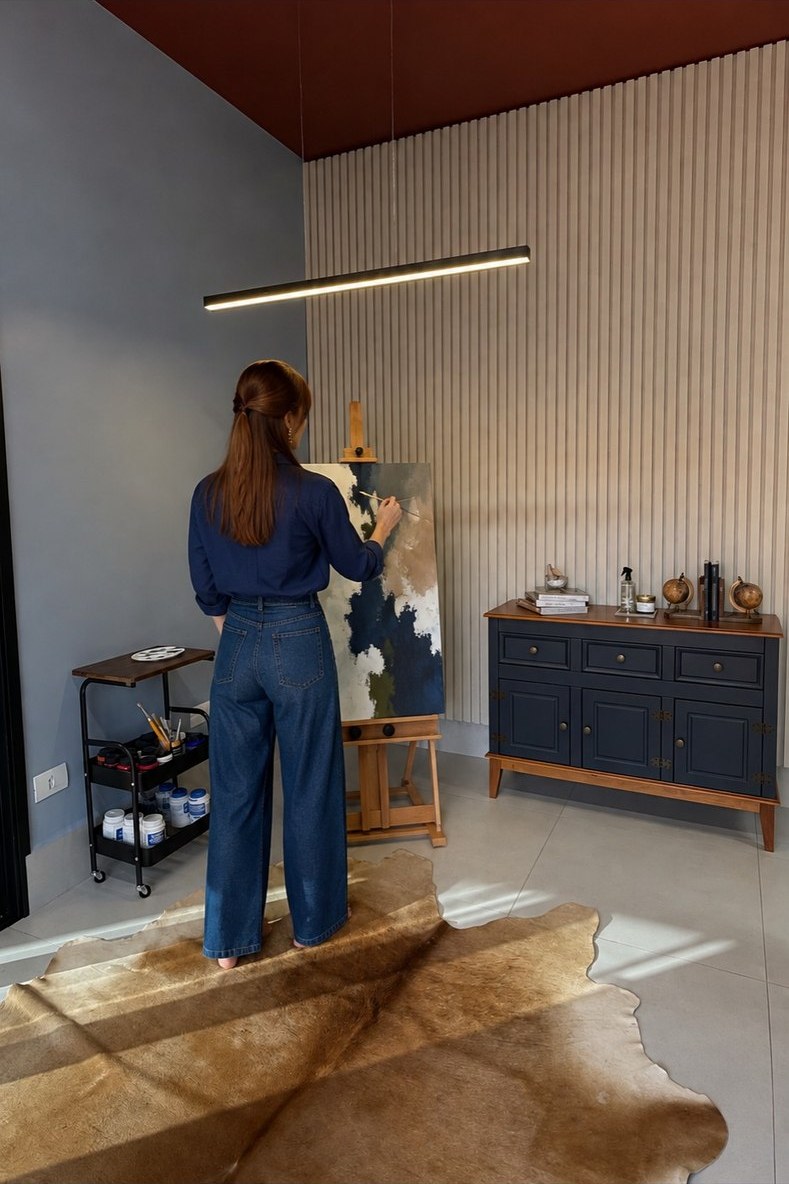 Nayara Pires pintando uma tela no cavalete, em seu ateliê