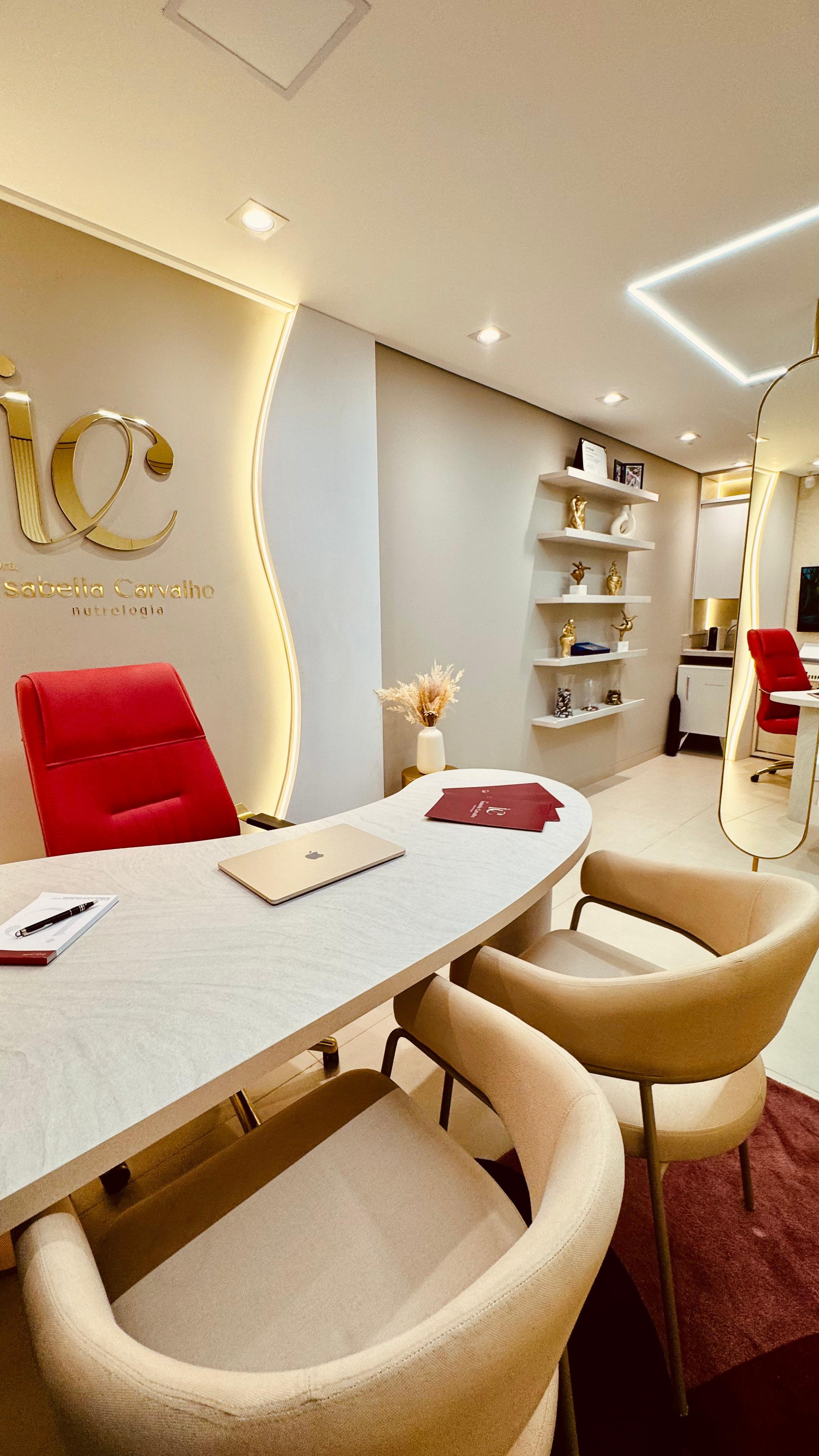 Clínica de Nutrologia Isabella Carvalho — sala de atendimento com logo integrado à parede, mesa oval e detalhes em dourado